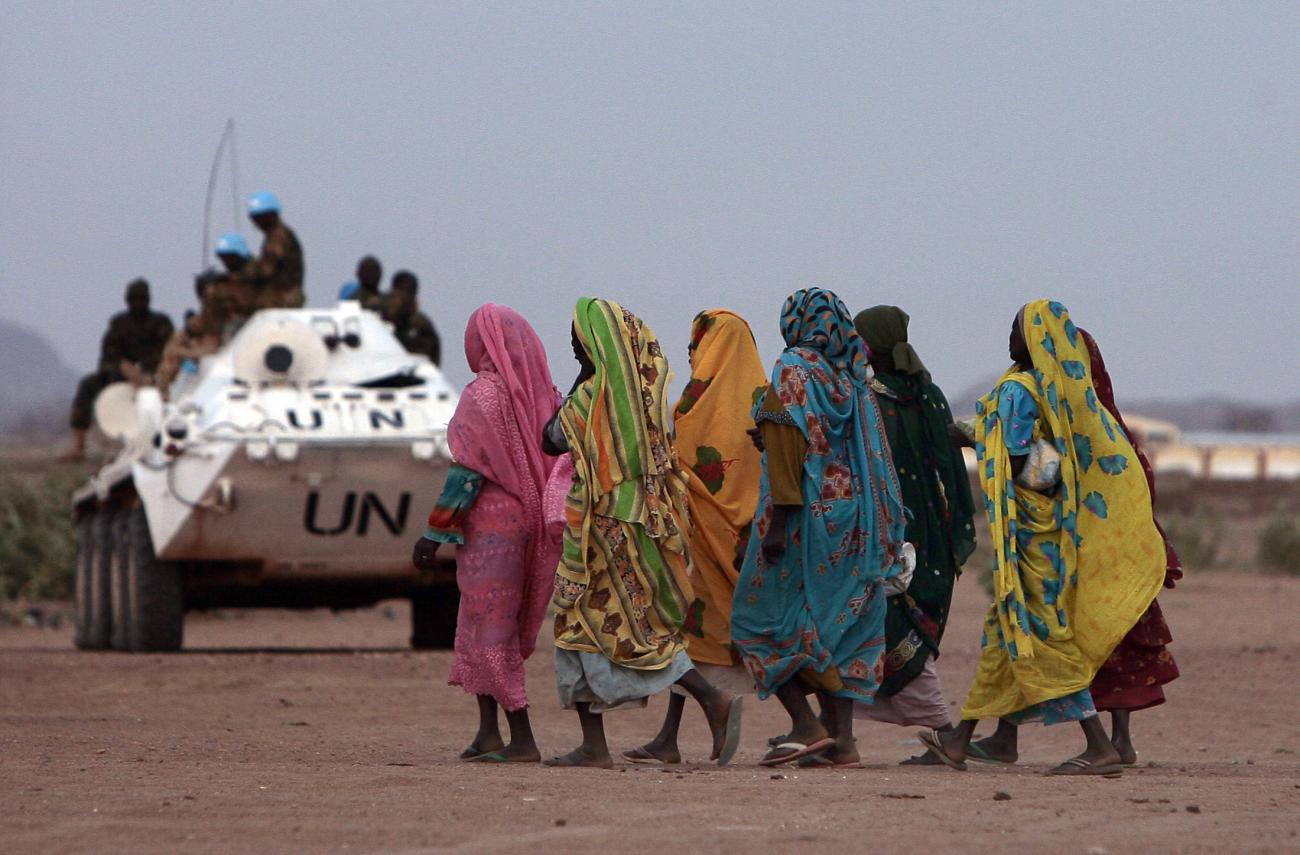 Displaced Sudanese women walk past an armoured personnel carrier (APC) of the United Nations-African Union Mission in Nyala, southern Darfur, on March 17, 2009.