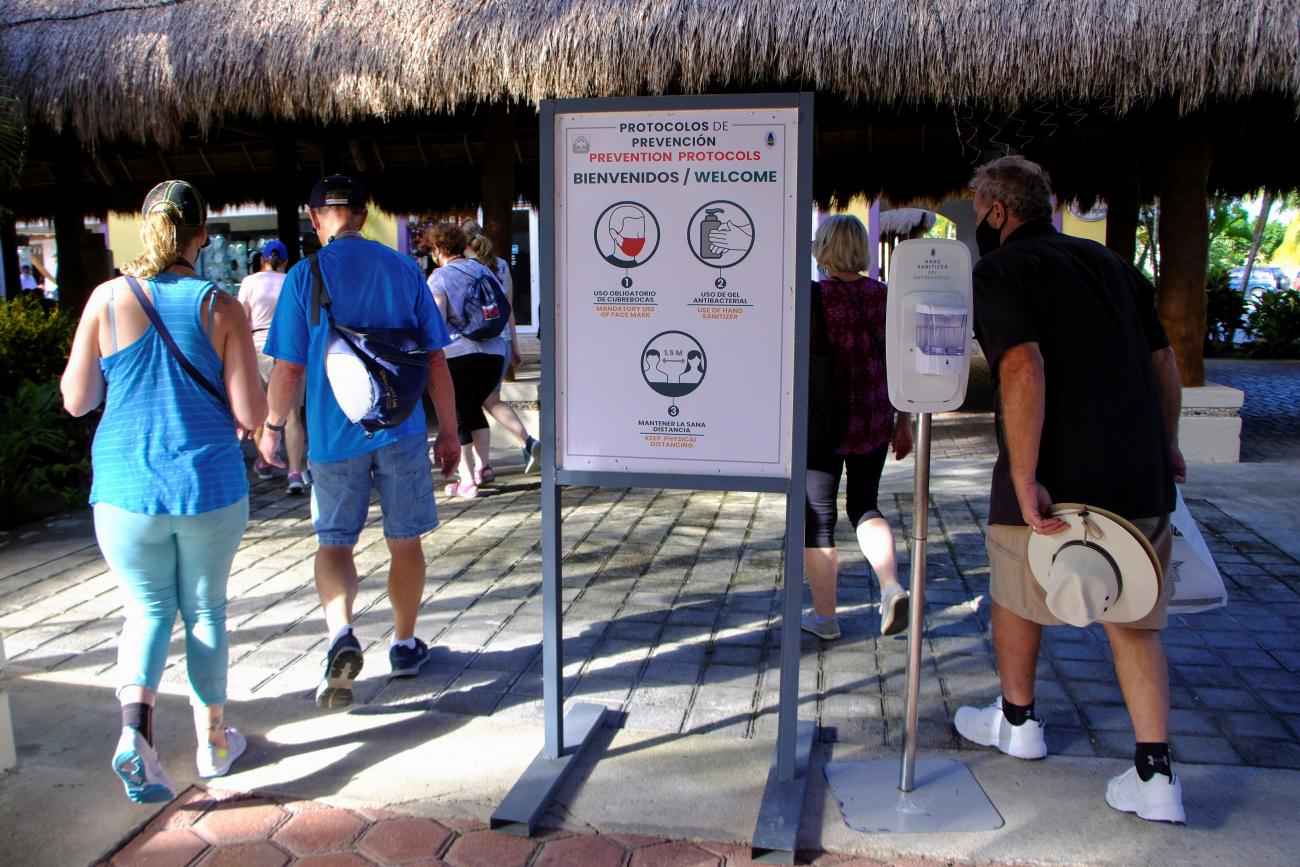 People walk past a sign with safety recommendations on the coronavirus disease (COVID-19) near a dock for cruise ships, in Cozumel, Mexico December 6, 2021. 
