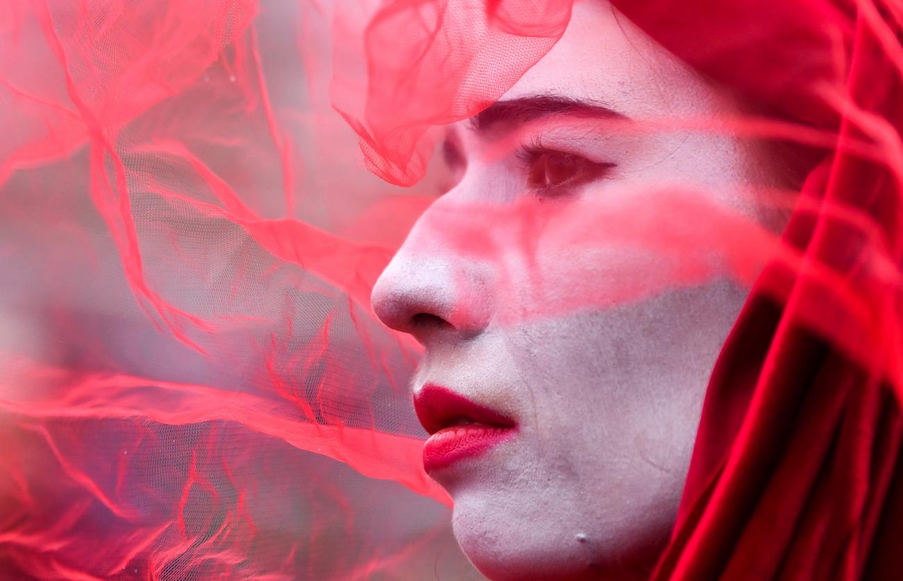 A member of Extinction Rebellion Red Rebel Brigade wears white face paint and a red veil as they take part in a protest during the UN Climate Change Conference (COP26) in Glasgow, Scotland, on November 12, 2021.