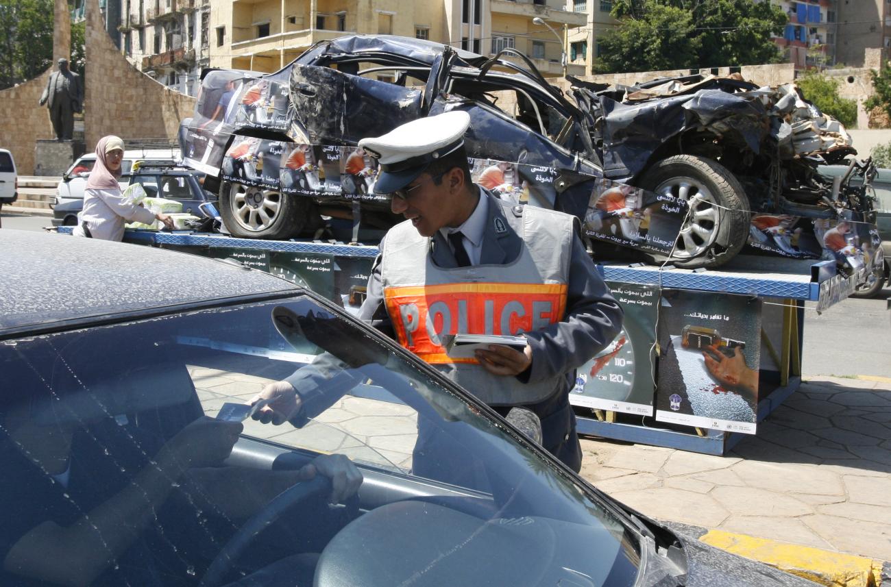 A policeman passes out leaflets with road accident statistics, in front of a destroyed car which is put on display, during a campaign to promote safe driving in Beirut April 25, 2007.