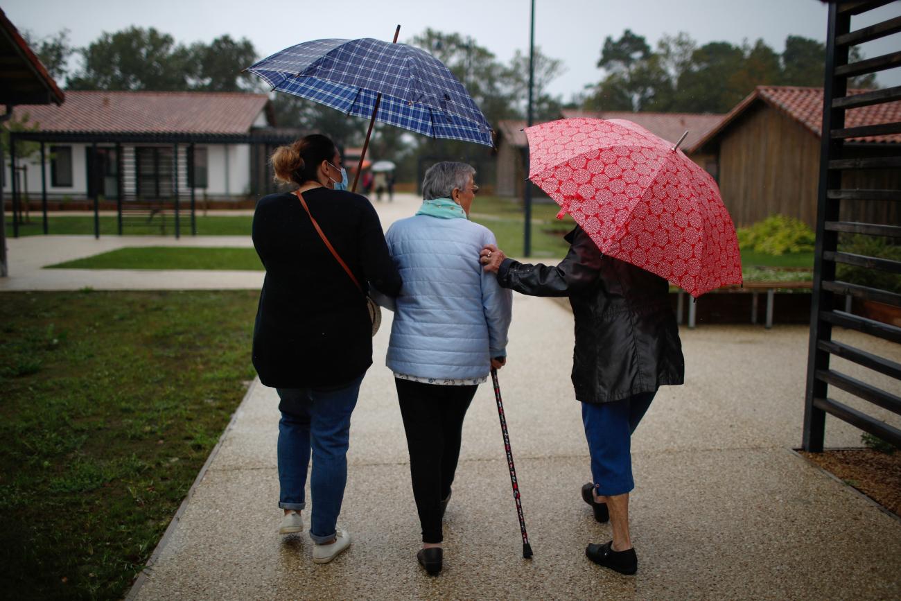 Alzheimer's patients with blue and pink umbrellas walk together around a village for people with dementia