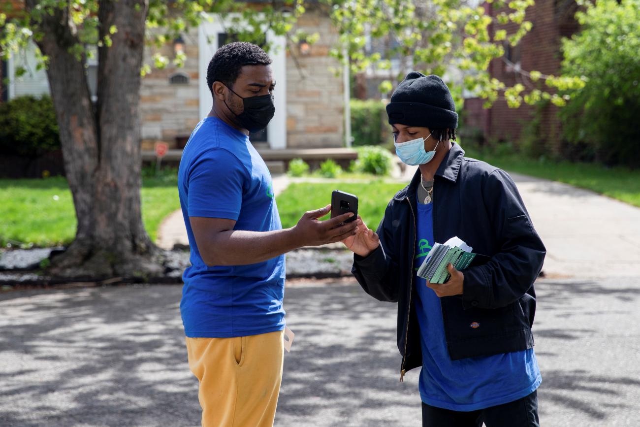 Volunteers from Better Men Outreach Robert Day and Deares Carey converse on the sidewalk as they keep track of which houses to knock on during a door-knock campaign to provide information about where people can get their vaccinations and help answer questions related to hesitancy around the coronavirus disease (COVID-19) vaccine in Detroit, Michigan