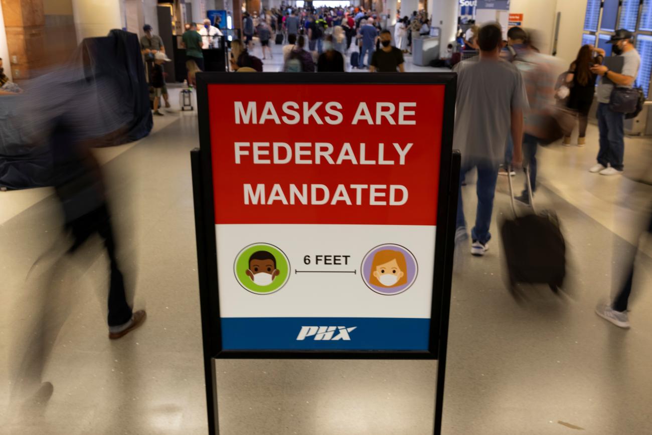 Travelers at Phoenix Sky Harbor International Airport make their way past a sign mandating face masks for all during the COVID-19 pandemic, on September 24, 2021.