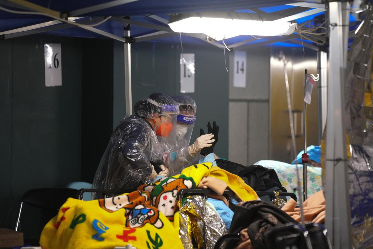 A woman holds the hand of a patient at a makeshift treatment area outside a hospital, during the COVID outbreak in Hong Kong, on February 17, 2022. 