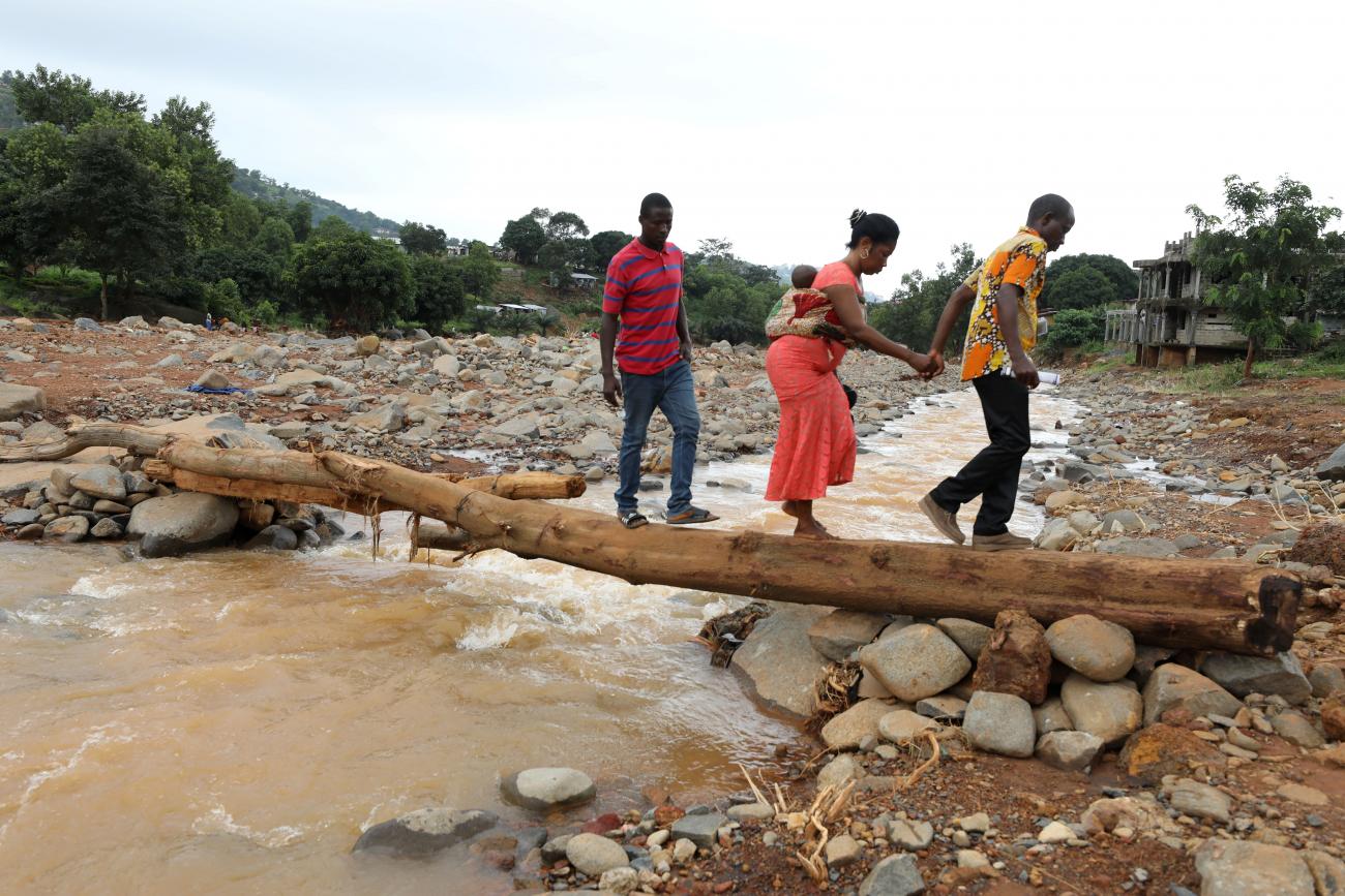 A man helps a woman cross a log bridge after the flash flood washed away a concrete bridge at Pentagon, in Freetown August 18, 2017