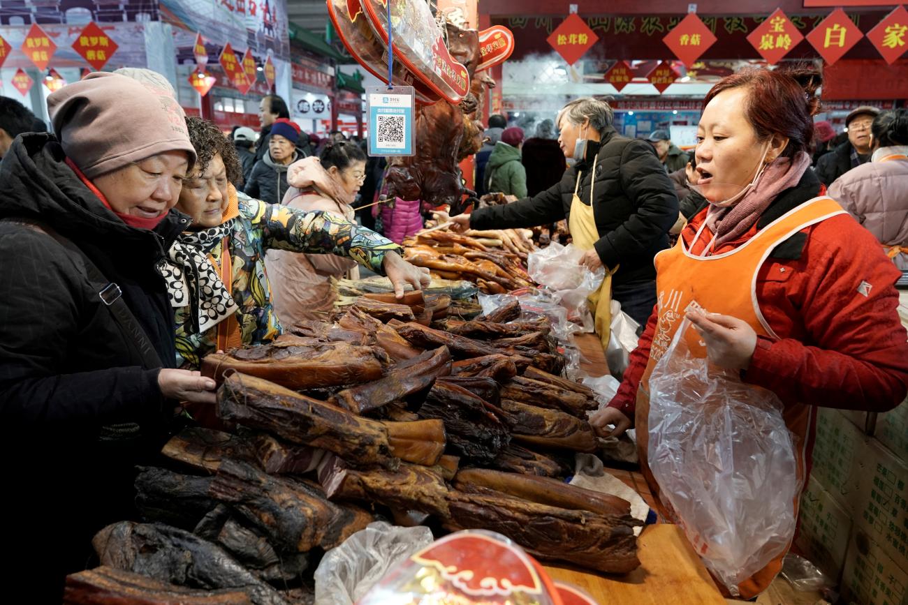 Customers select pork from a market stall laden with meat and decorated for Chinese New Year