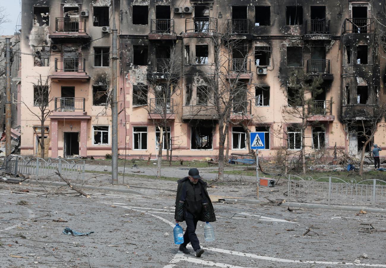 Cut off from water, a local resident carries bottles of water as he walks past a building charred and heavily damaged during Russia’s attack on Ukraine's southern port city of Mariupol. Photo taken on April 3, 2022.