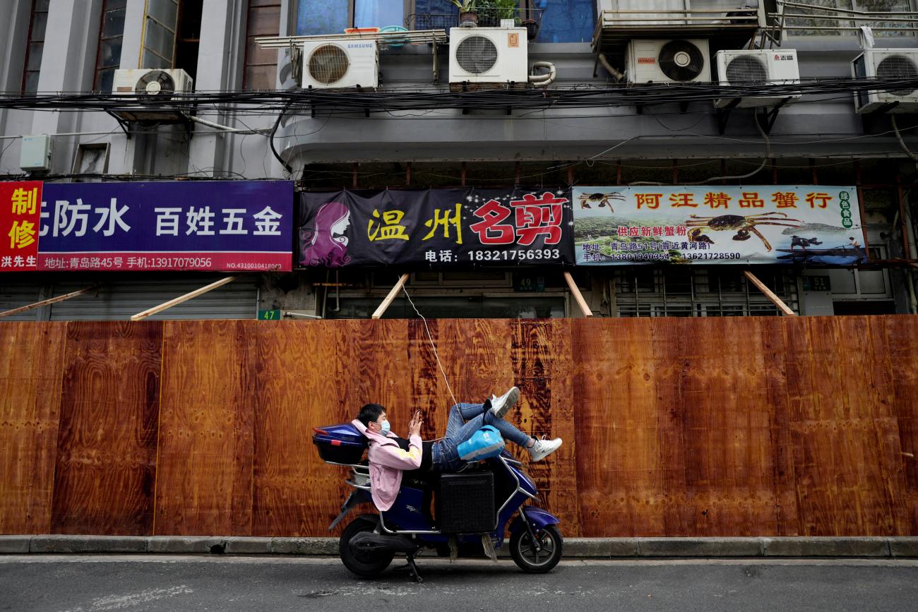 A man uses a mobile phone while leaning on a scooter in front of barricades of a sealed-off area, following the coronavirus disease (COVID-19) outbreak in Shanghai, China March 30, 2022.
