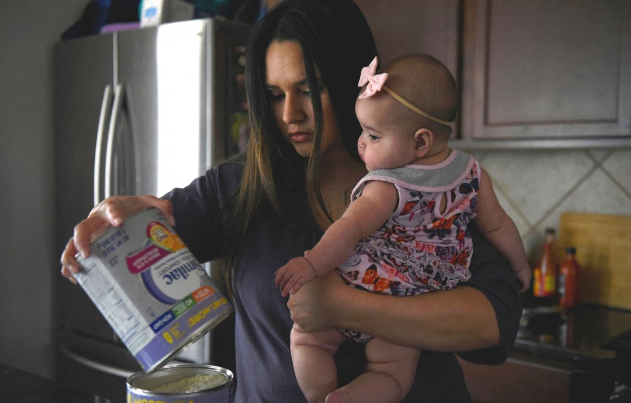 A mother with long brown hair holds her baby daughter, who is wearing a pink bow in her arms as she consolidates her last jar of baby formula amid continuing nationwide shortages in Houston, Texas, U.S., May 19, 2022.