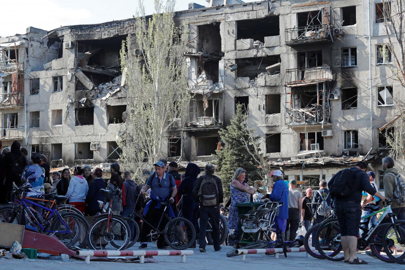 Local residents with bicycles gather to receive humanitarian aid during Russia's invasion of Ukraine against a background of bombed apartment buildings with blackened window frames in the southern port city of Mariupol, Ukraine April 28, 2022. 