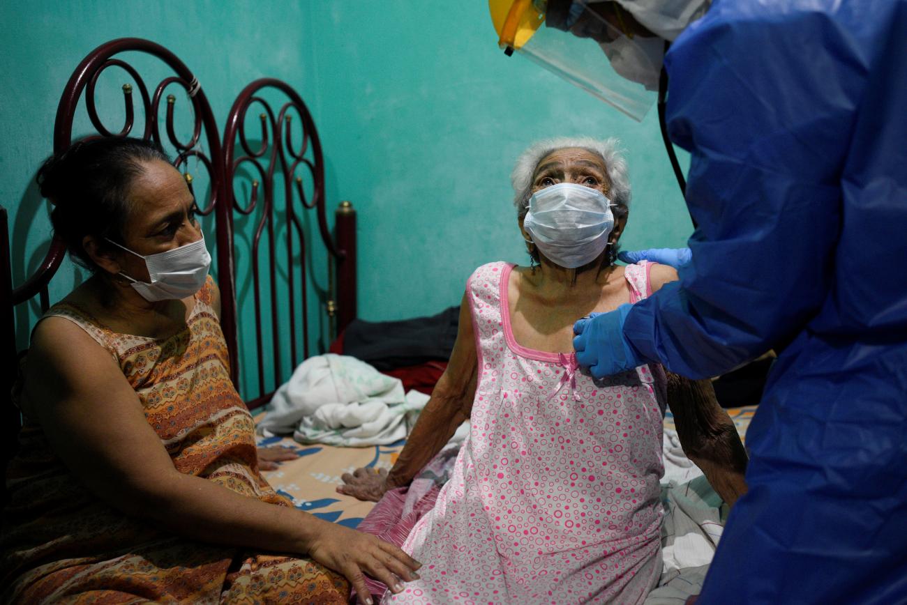 A 77-year-old woman in and orange dress and face mask cares for her 94-year-old mother in a pink nightgown is given a medical examination by doctors from the Ecuadorian health ministry's rapid response team for COVID-19 at their home with green walls in Guayaquil, Ecuador April 29, 2020.