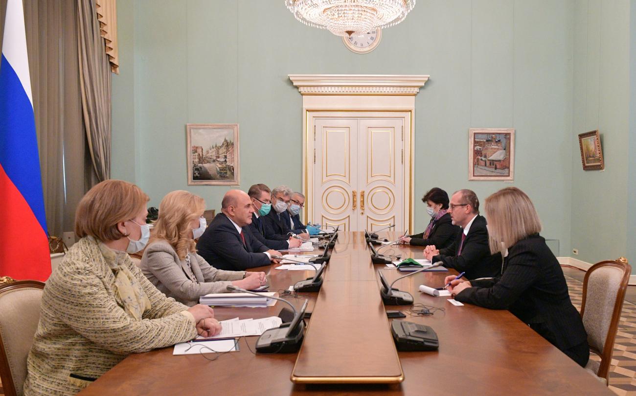 Russian Prime Minister Mikhail Mishustin and a Russian delegation sit on the right side of a long wooden table at a meeting with Hans Kluge, World Health Organization regional director for Europe, and his team, who sit on the opposite side of the table in Moscow, Russia September 23, 2020. 