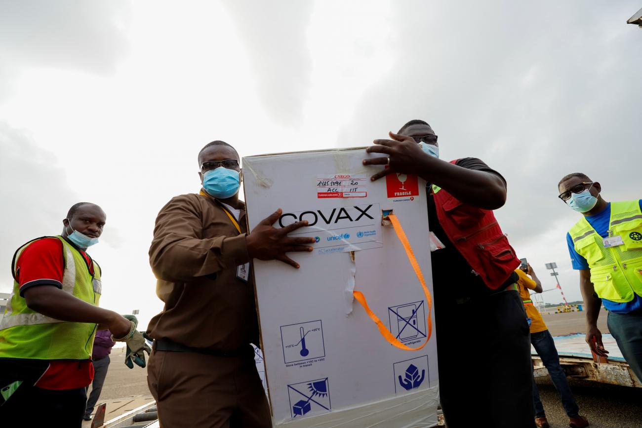 Workers in highlighter yellow vests carry boxes of Oxford/AstraZeneca COVID-19 vaccines, redeployed from the Democratic Republic of Congo, at the Kotoka International Airport in Accra, Ghana, on May 7, 2021. 