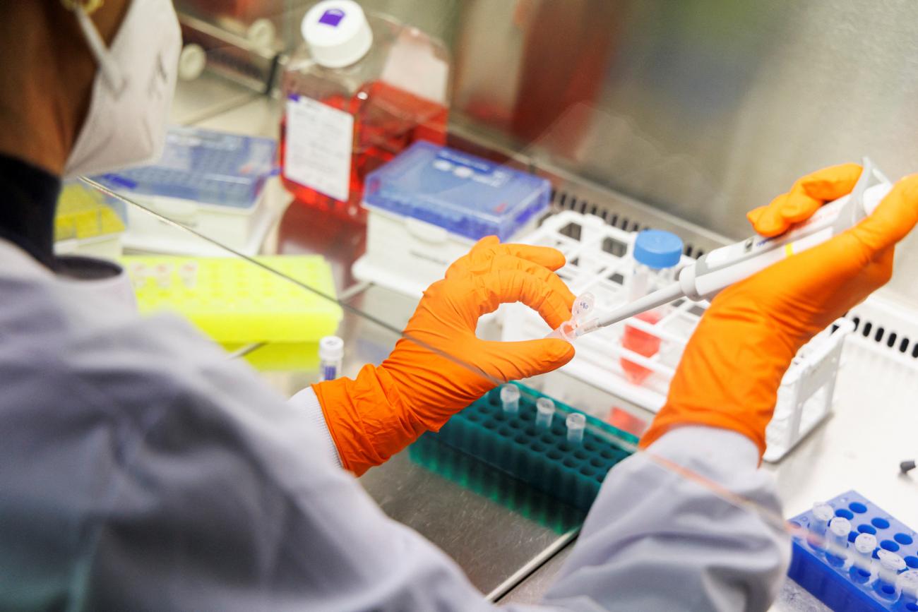 An employee wearing orange gloves and personal protective equipment holds a medical device in a laboratory.