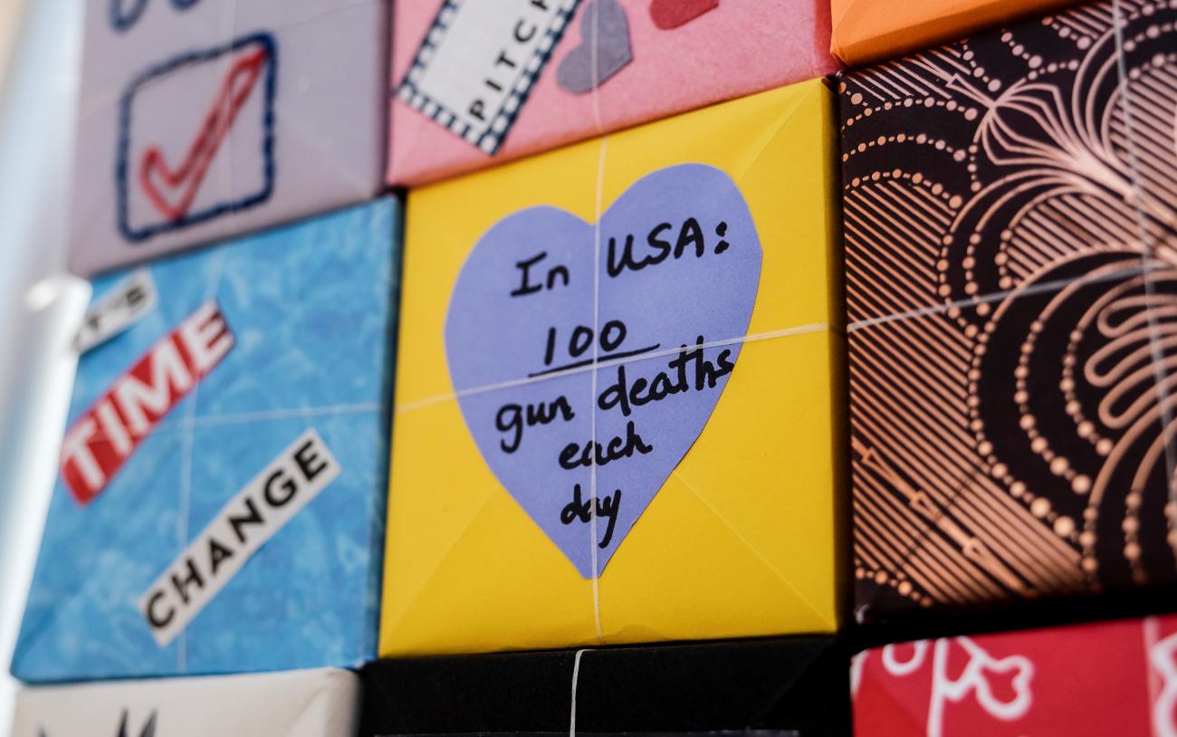 A stack of colorful paper boxes with messages like "Time for Change" and "In the USA 100 gun deaths each day"