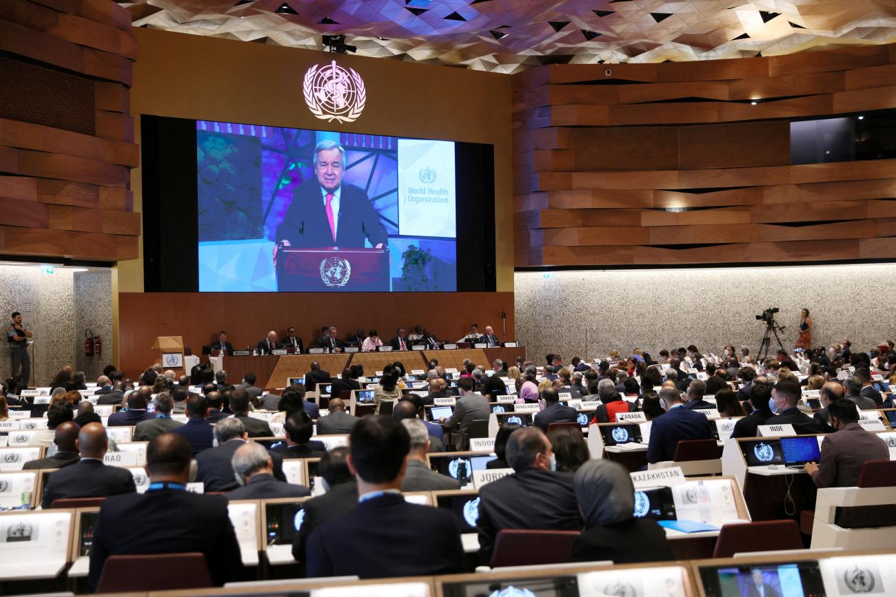 His image projected on a large screen at the front of the vast meeting room, UN Secretary-General António Guterres addresses the 75th World Health Assembly at the United Nations in Geneva, Switzerland, on May 22, 2022. 