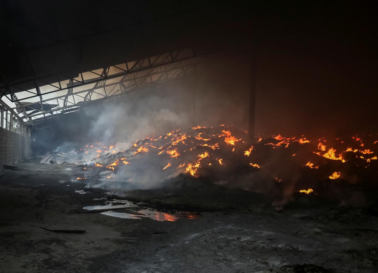 Inside the dark interior of a grain silo a huge pile of seeds burn, appearing like hot orange coals, below a roof that has been partially destroyed by shelling during Russia's attack on Ukraine. Photo was taken in the Donetsk region of Ukraine, on May 31, 2022. 