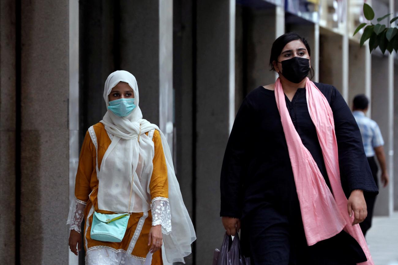 Two women wearing long dresses and scarves, and carrying their purses, walk outside a market amid a rise in COVID-19 cases in Karachi, Pakistan, on June 27, 2022. 