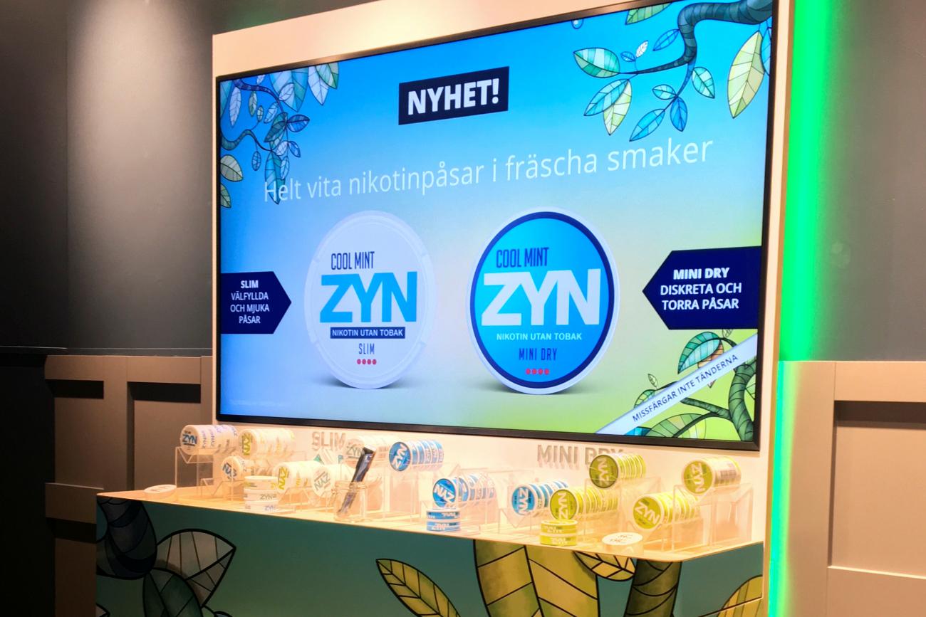 a digital kiosk advertises ZYN nicotine pouches, using light blue graphic design, at a store in Stockholm, Sweden