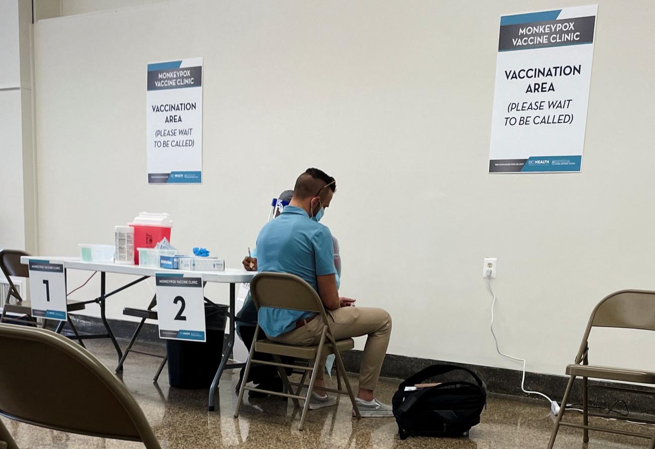 A man wearing a teal shirt turns his back to the camera as he receives a monkeypox vaccine