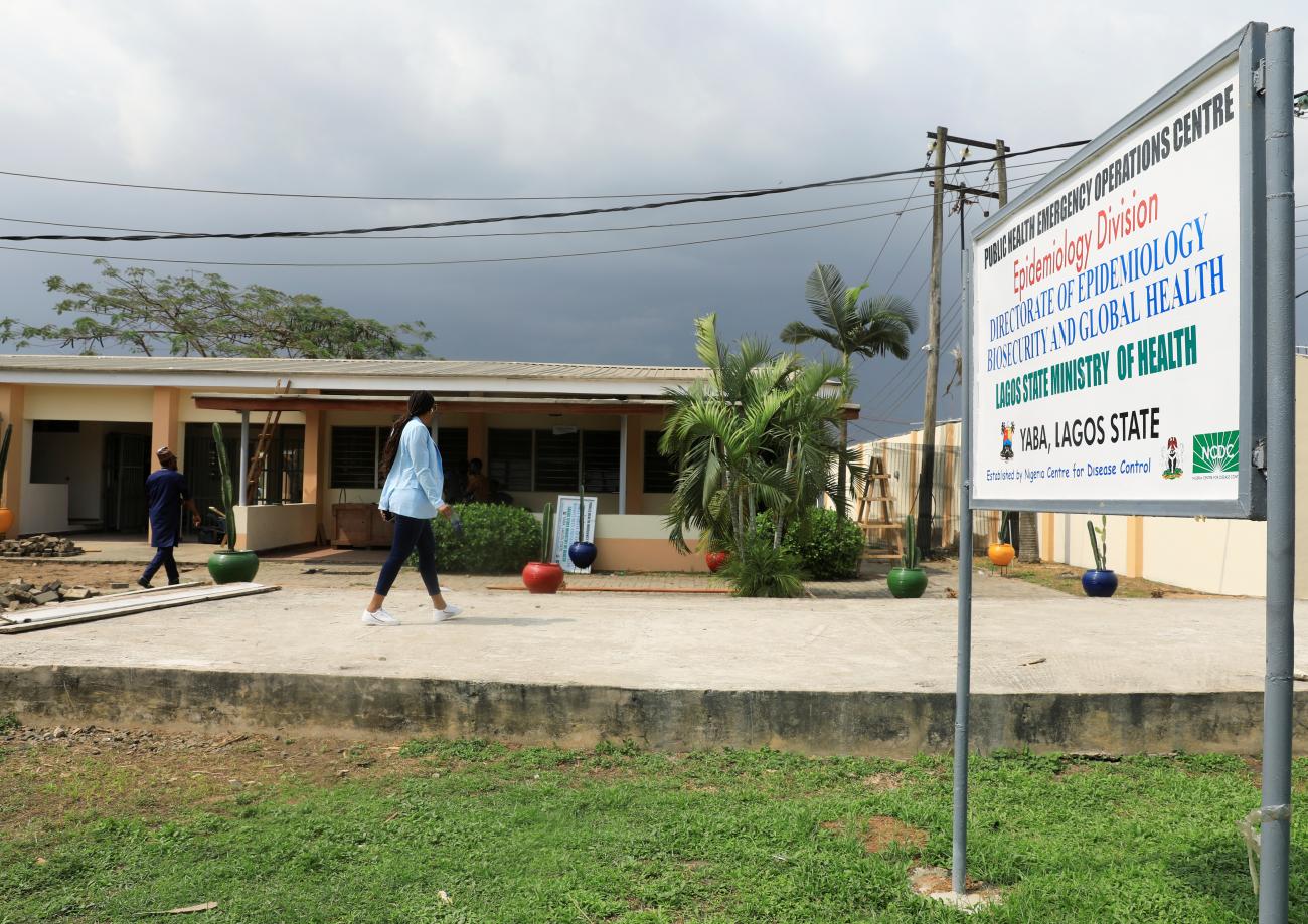 A woman with a long black ponytail wearing a light blue shirt and black slacks walks in front of the Public Health Emergency Operations Centre at the mainland hospital in Yaba, Lagos, Nigeria, on March 6, 2020. 