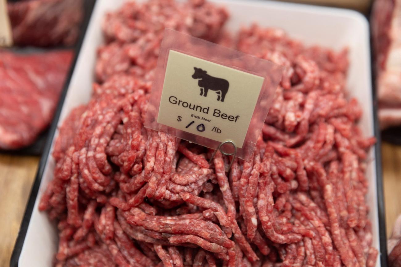 A photo of uncooked ground beef in a butcher's display with a small laminated tag that reads "ground beef" and has a small black outline of a cow