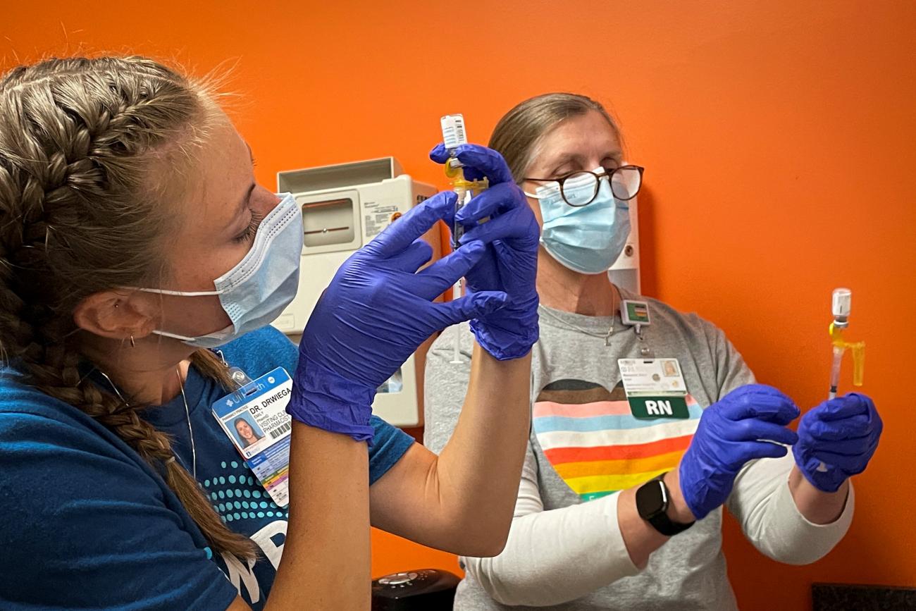 Health-care workers, wearing t-shirts with a heart filled in with the colors of LGBTQ+ pride prepare monkeypox vaccines in a clinic with orange walls
