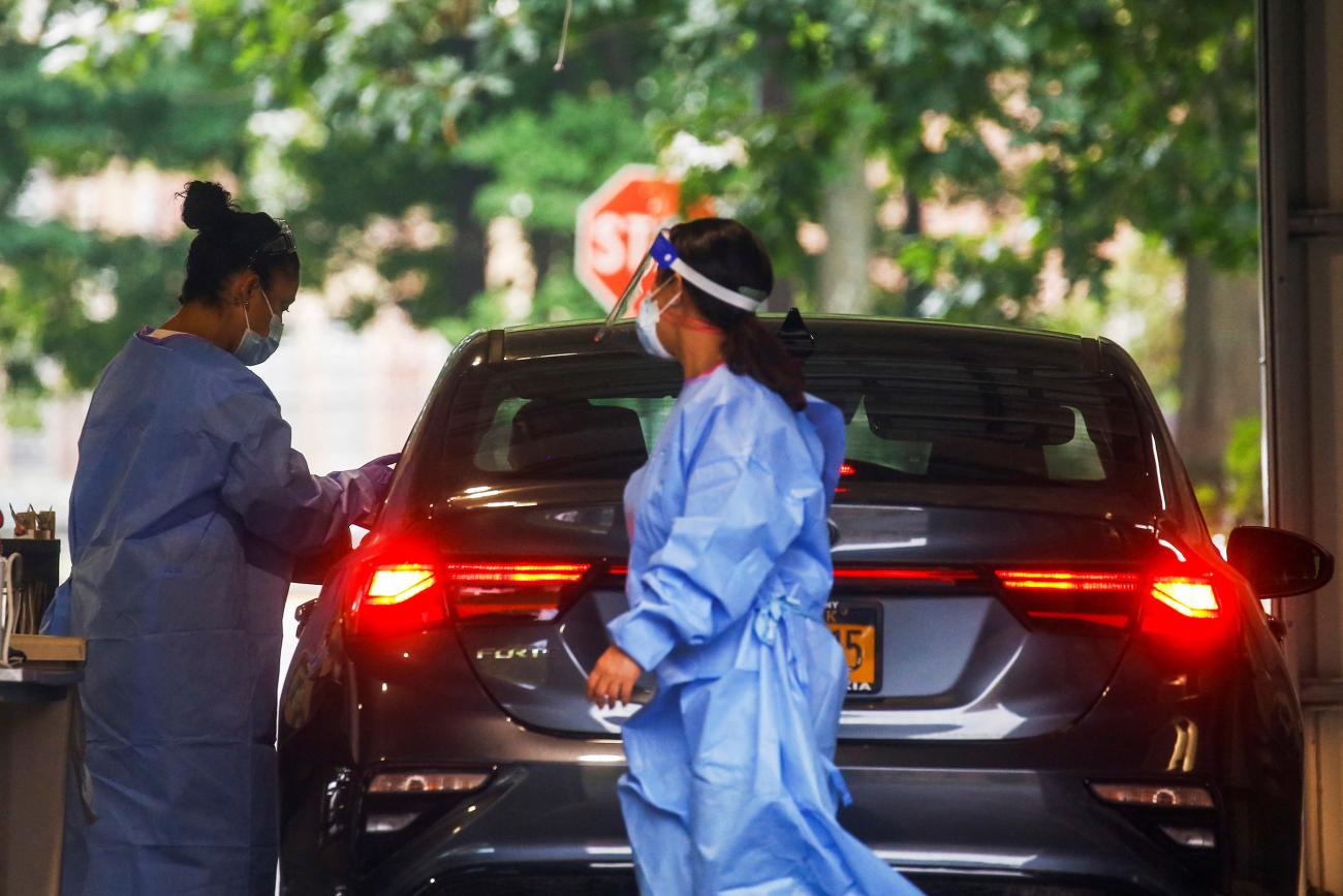 Health workers in blue gowns attend to patients at a drive-through monkeypox vaccination point shaded by tall green trees in Valhalla, New York, the day before New York issued a public health emergency declaration, on July 28, 2022. 