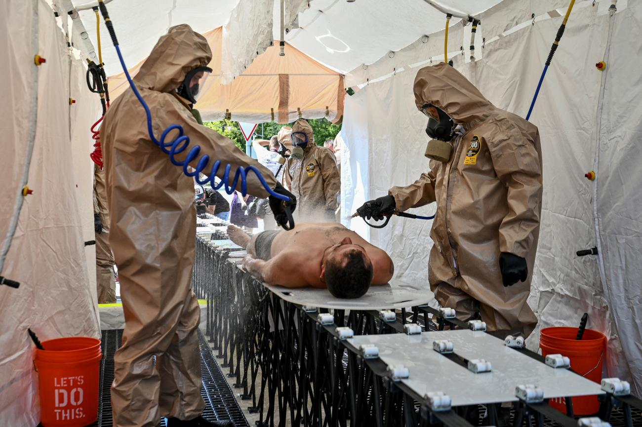 Members of the Ukrainian State Emergency Service wearing beige protective suits rinse a shirtless man with special hoses in a tent as part of nuclear disaster response drills amid shelling of Zaporizhzhia Nuclear Power Plant, as Russia's attack on Ukraine continues, in Zaporizhzhia, Ukraine on August 17, 2022. 