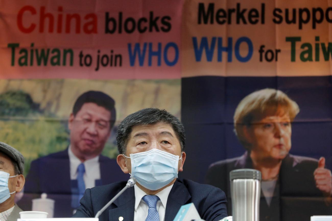 Taiwan's Health Minister Chen Shih-chung appears wearing a blue surgical face maskseated in front of orange banners that read "China blocks Taiwan to join WHO" at a new conference, in Taipei, Taiwan, on May 15, 2020