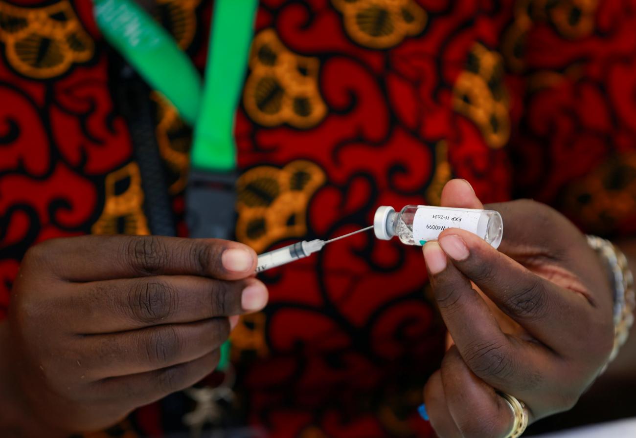 A close-up image shows just the hands of a health worker who is dressed in a coloreful orange and red African shirt and is taking a COVID-19 vaccine dose from a vial during a mass vaccination rollout in Abuja, Nigeria, on November 19, 2021.