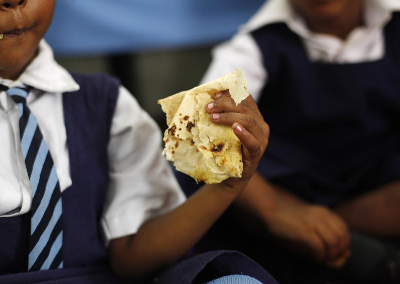 A close-up photo of the hand of a schoolgirl in a uniform (no face showing) about to eat flat bread during her midday meal, food distributed by a government-run primary school, in New Delhi, India. 