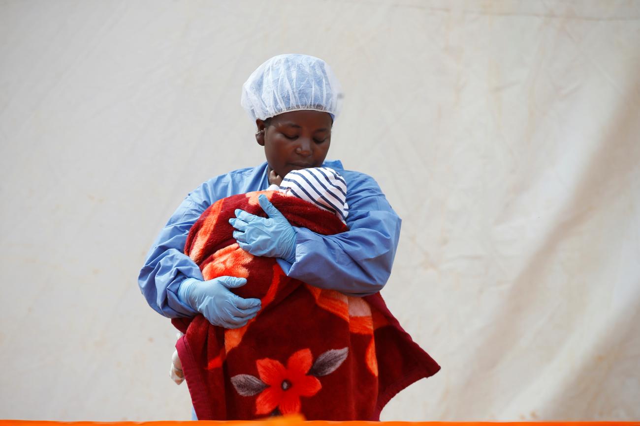Dressed in blue scrubs, Rachel Kahindo, an Ebola survivor and caregiver, holds a baby with Ebola who is wrapped in red and orange fabric as she stands outside the Ebola treatment center in Butembo, Democratic Republic of Congo, on March 25, 2019. REUTERS/Baz Ratner