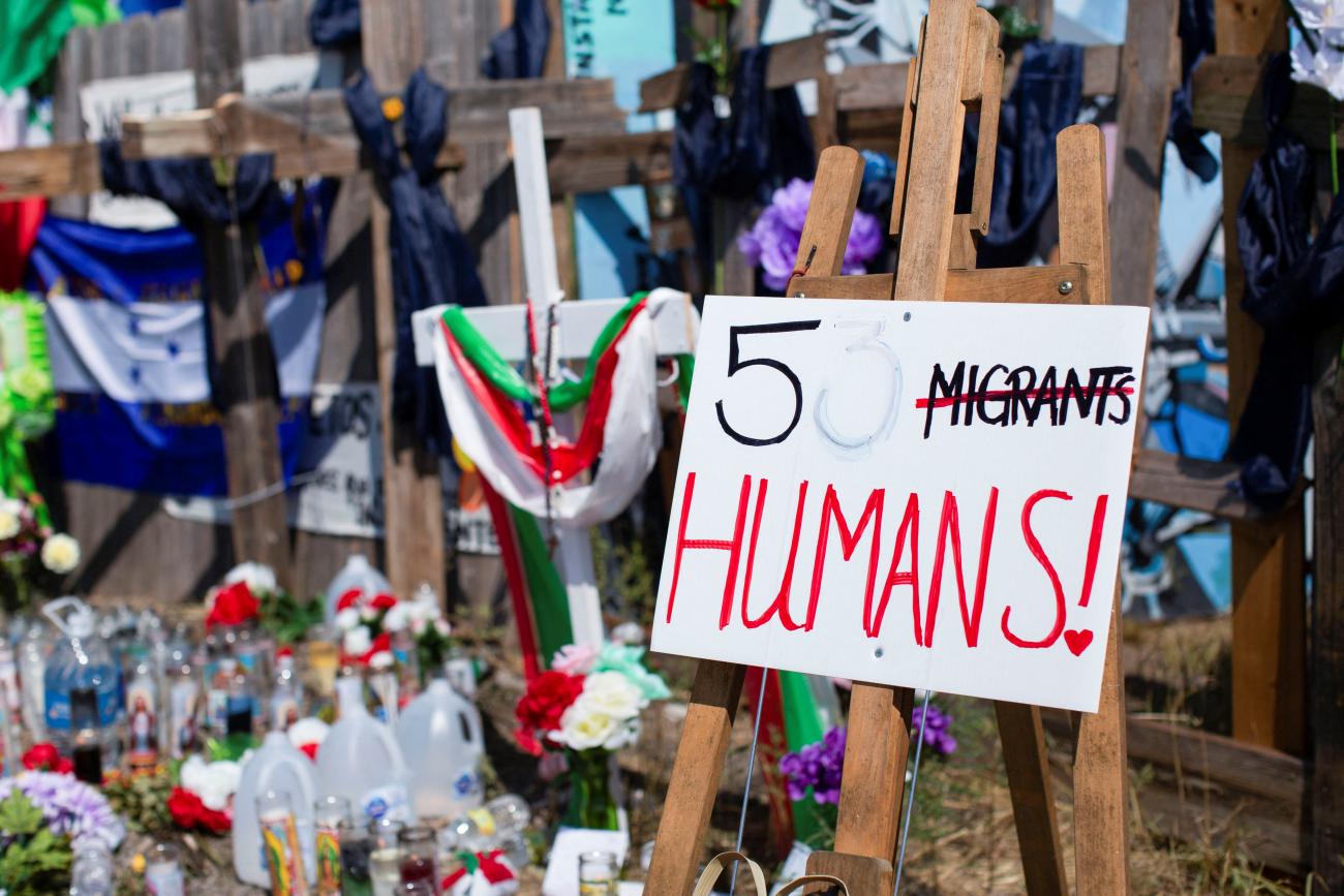 A memorial for people, including children, who died inside a trailer truck in San Antonio, Texas, on June 30, 2022. The memorial includes crosses and a sign that says "53 Migrants," with the word "Migrants" crossed out and replaced with the word "Humans."