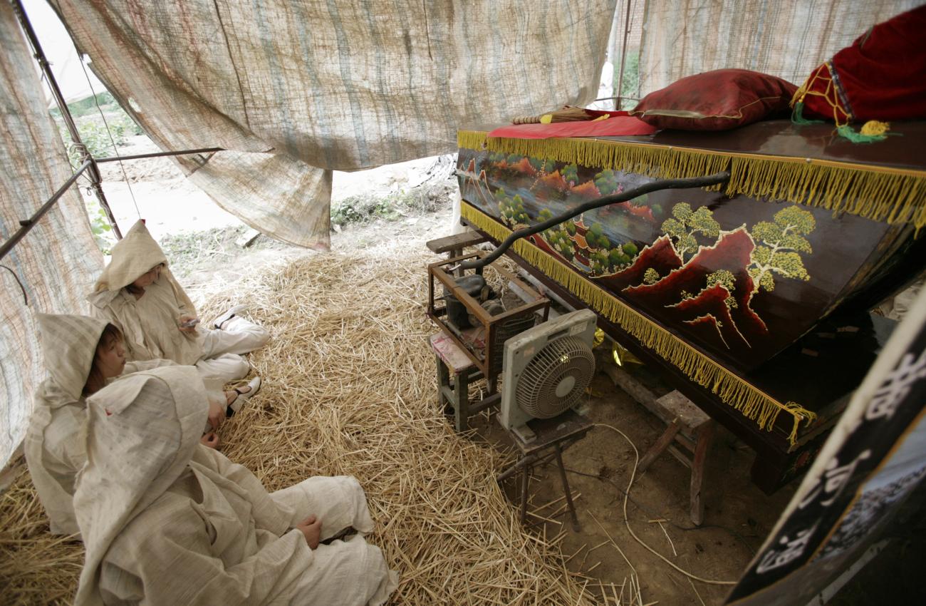 A mourner uses her mobile phone beside the coffin, which is being kept cold by a cooling apparatus, in a funeral tent outside their home during a traditional rural Chinese funeral at Bei Xue village, China's Shanxi province July 8, 2007.Even as China makes giant economic and social leaps forward, tradition lives on in rural areas. REUETERS/Reinhard Krause (CHINA)