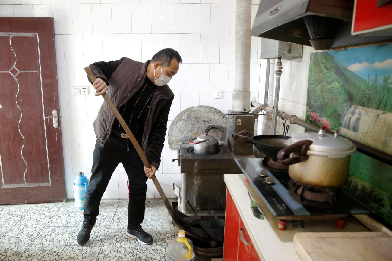 A man shovels coal into a tray next to an oven he uses to heat his home in his kitchen in the village of Heqiaoxiang outside of Baoding, Hebei province, China, December 5, 2017. Picture taken December 5, 2017. REUTERS/Thomas Peter