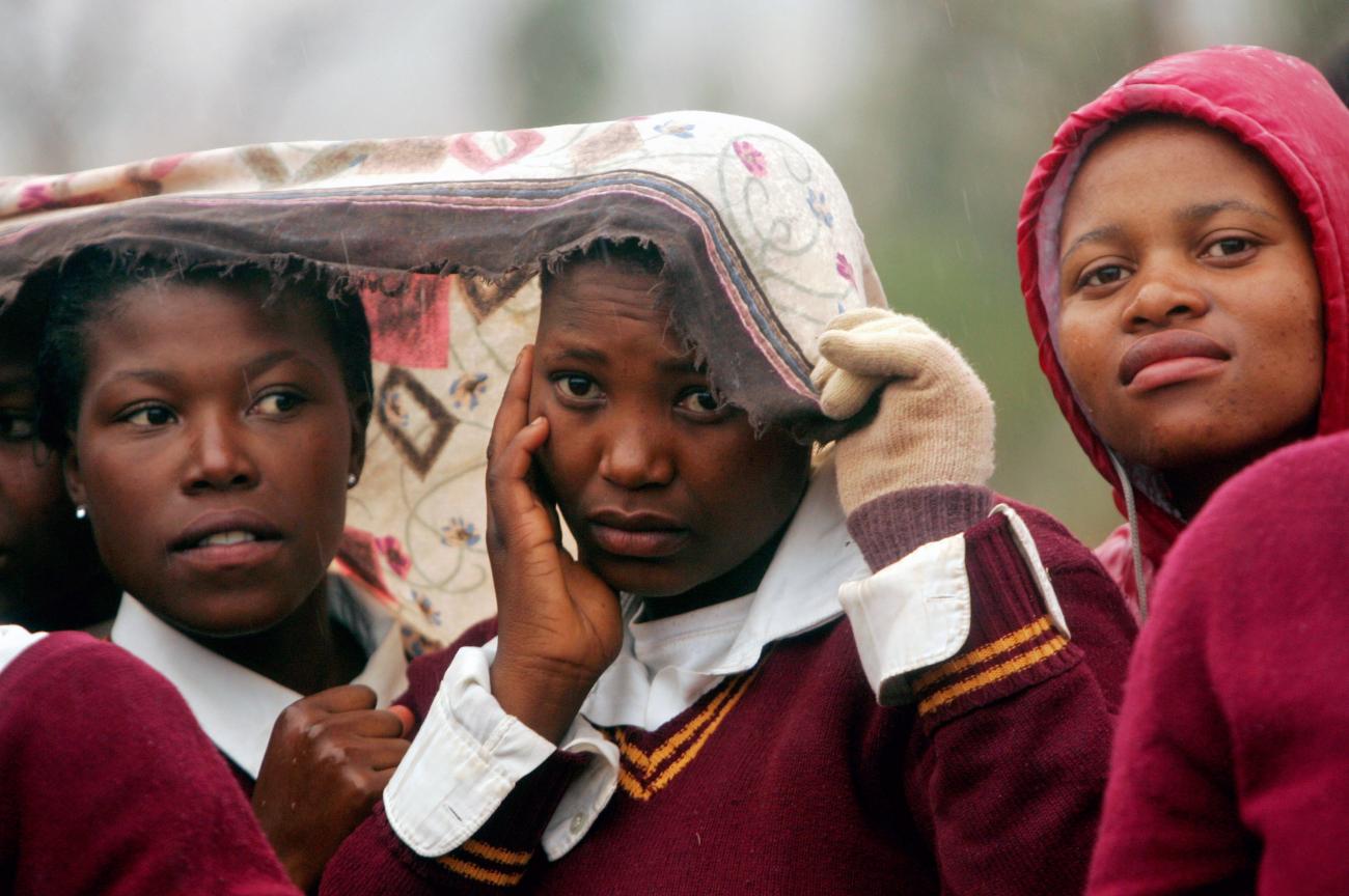 School children listen in the falling rain as Irish rock star Bono talks at a school in Butha Buthe, near Lesotho's capital Maseru, May 17, 2006. Bono is on the first leg of a six-nation African tour which aims to highlight the progress so far in providing treatment to people living with HIV and AIDS. REUTERS/Mike Hutchings