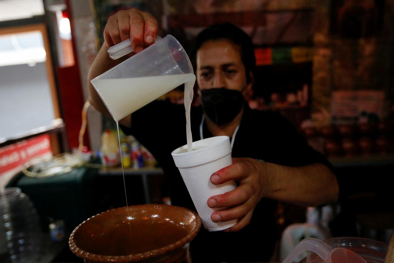 A bartender pours Pulque, a traditional pre-Hispanic alcoholic beverage fermented from the maguey plant, to customers in a stall at the Pulque Fest, a festival to promote the drink, in Mexico City, Mexico, on April 2, 2022.
