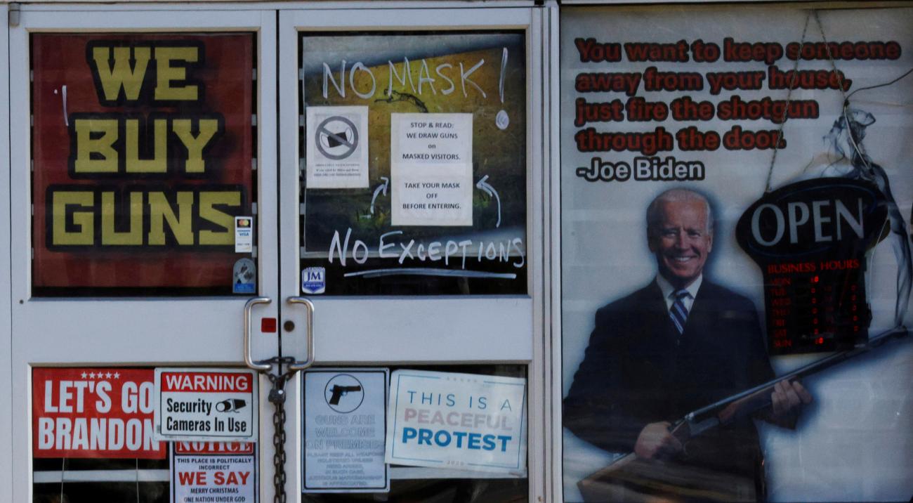A sign warning customers not to wear a face mask hangs next to a poster advocating against gun control and depicting U.S. President Joe Biden at the 619DW Guns and Ammo store