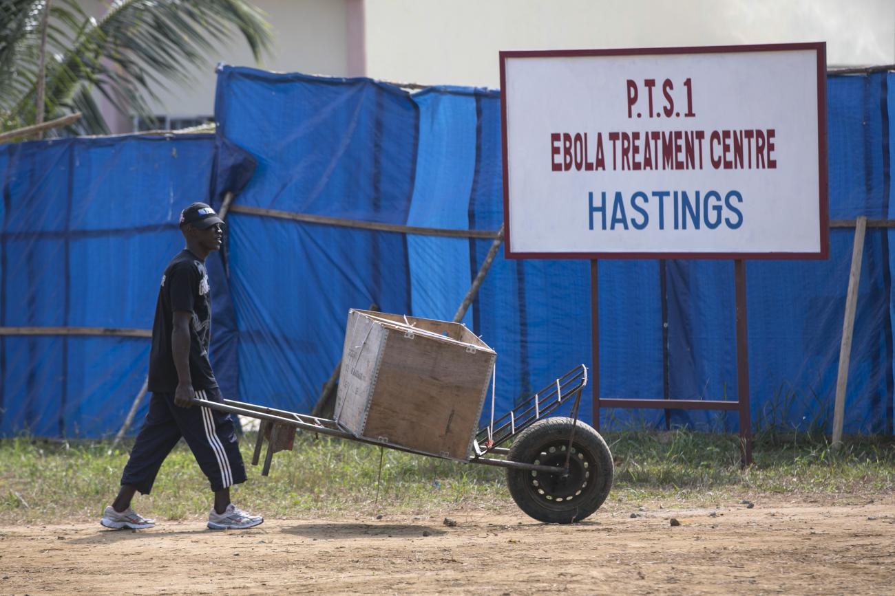 A man pushes a wheelbarrow past the entrance to the Hastings Ebola treatment center in a neighborhood in Freetown, Sierra Leone, on December 21, 2014.