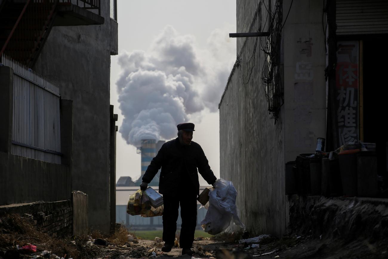 A man collects recyclablesr from an alley as smoke billows from the chimney of a factory in rural Gaoyi county, known for its ceramics production, near Shijiazhuang, Hebei province, China, December 7, 2017.