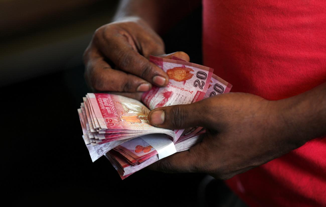 Close up image of the hands of a South Asian man wearing a red shirt counting rupees. 
