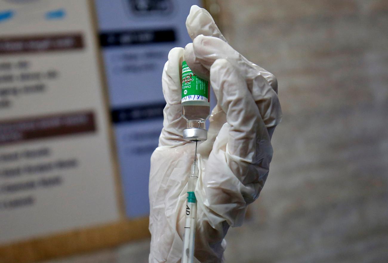 A hand holds a vaccine vial as the liquid is extracted into a syringe.