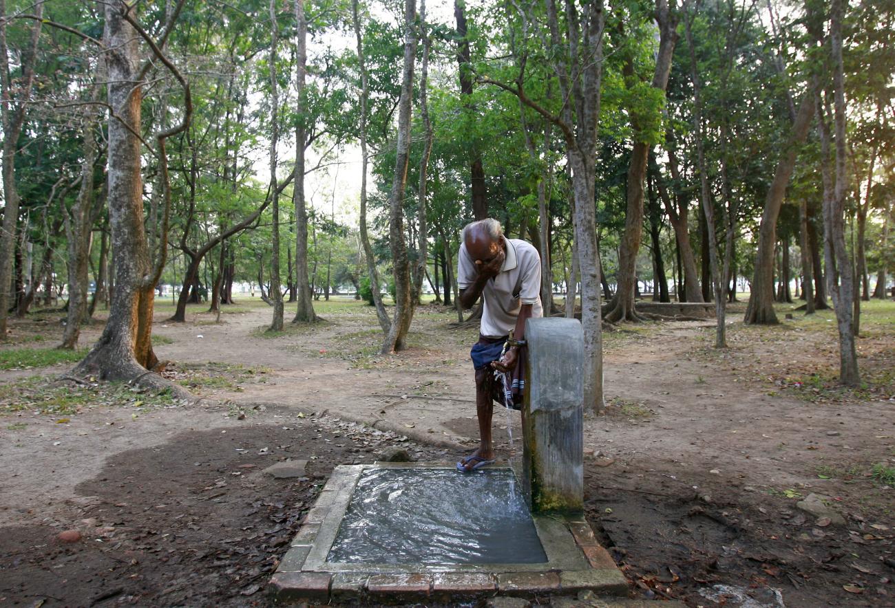 A man washes his face at a tap in a public park.