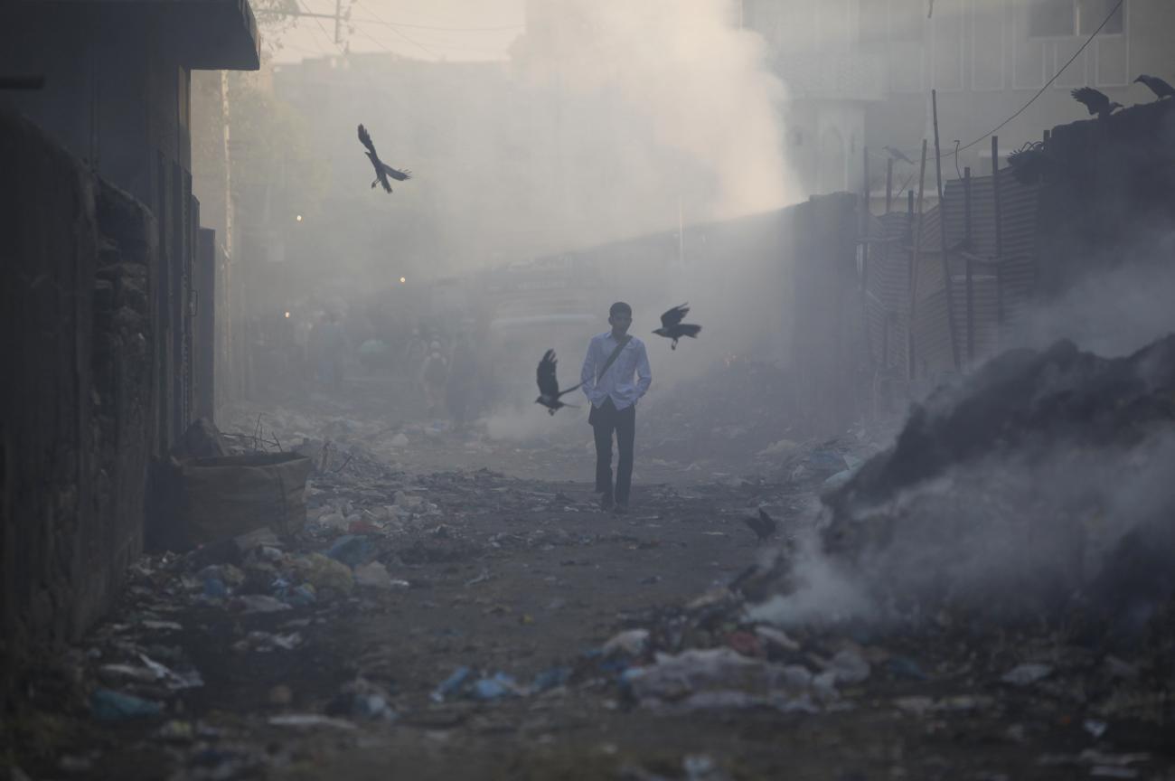 A boy walks through an alley littered with the pile of smouldering waste, while heading to school during early hours of the morning