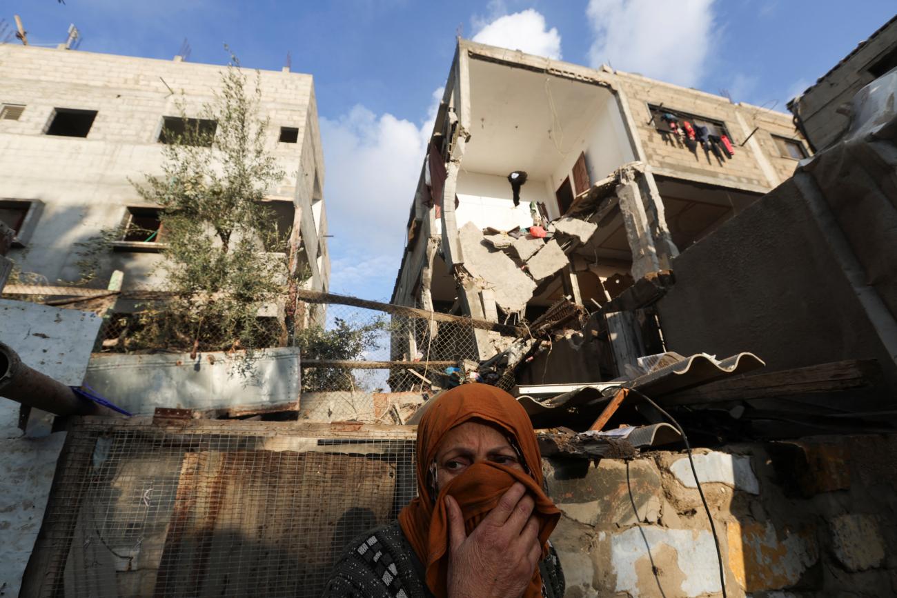 A Palestinian woman stands in front of a house damaged in an Israeli strike.