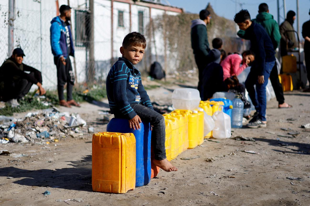 A displaced Palestinian boy, who fled his house due to Israeli strikes, sits on a water canister at a tent camp.