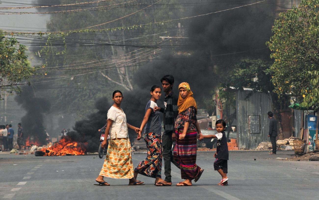 People walk on a street as barricades burn behind them during a protest against the military coup