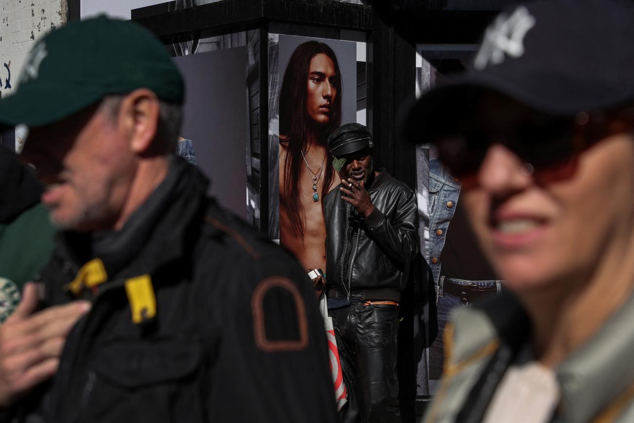 A man smokes a cigarette while people wait to cross a street