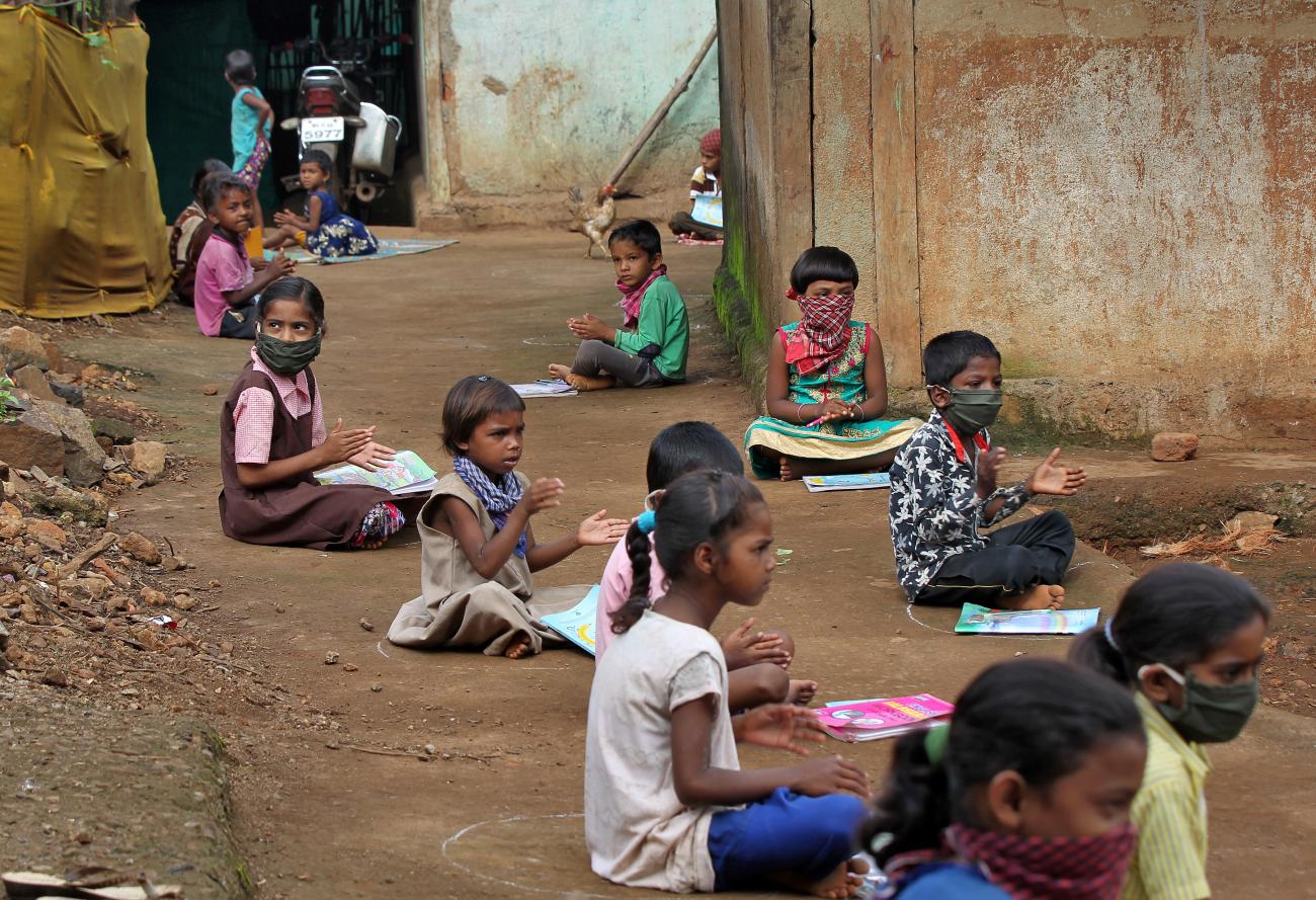 Children, who have missed their online classes due to a lack of internet facilities, sit on the ground.
